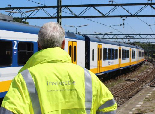 Inspecteur leefomgeving en transport die naar een voorbijrijdende trein kijkt